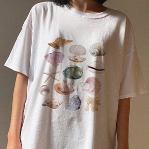 May include: White oversized t-shirt with a graphic print of various seashells in different colors and shapes.