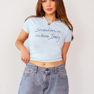 May include: A light blue t-shirt with the text "Somewhere in northern Italy" written in blue cursive script.