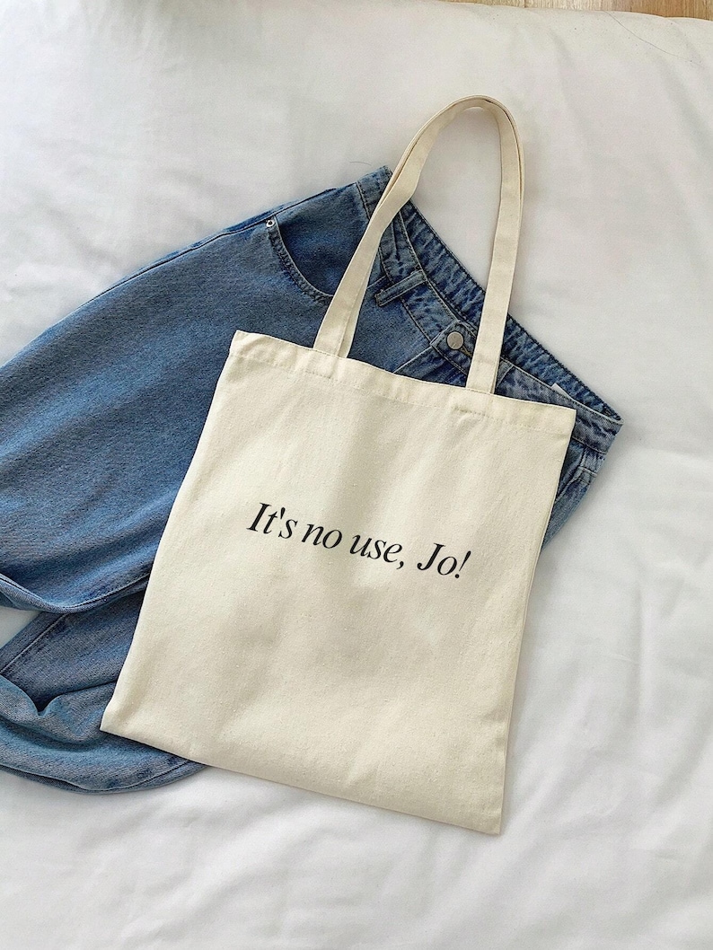 Pode incluir: Uma bolsa tote de lona bege com al&ccedil;as pretas e o texto "It's no use, Jo!" impresso na frente.