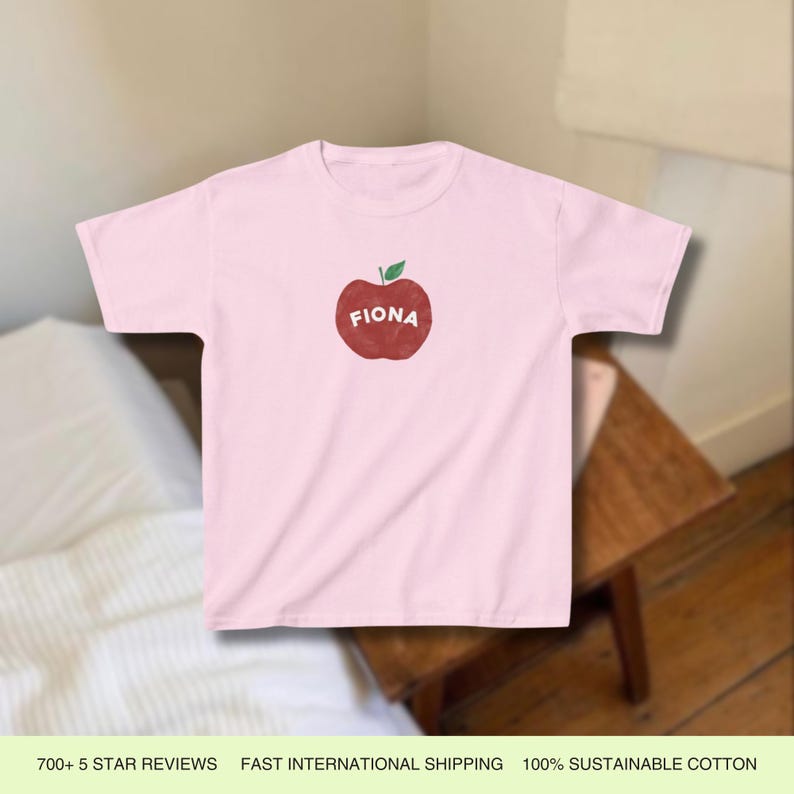 Pu&ograve; includere: Maglietta rosa con un grafico di una mela rossa e il nome "Fiona" stampato su di essa.