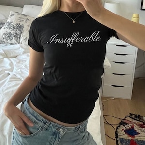 May include: A black t-shirt with the word "Insufferable" written in white cursive lettering.