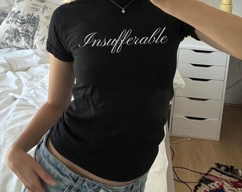 以下が含まれることがあります： 白い筆記体で「Insufferable」と書かれた黒いTシャツ