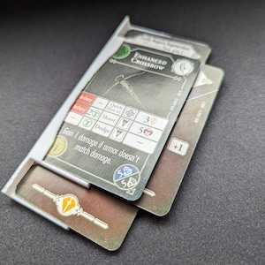 May include: A card game card with the text "Enhanced Crossbow" and a picture of a crossbow. The card has a green background and a white border. The card has a number of stats, including "Quick Shot x1", "Shoot", and "Dodge". The card also has a +1 bonus.