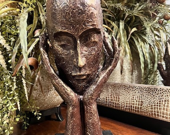 bronze-toned sculpture depicting contemplative face resting on hands