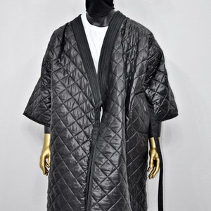 May include: A black quilted robe with a long, open front and a tie belt. The robe has a diamond pattern and is worn over a white t-shirt.