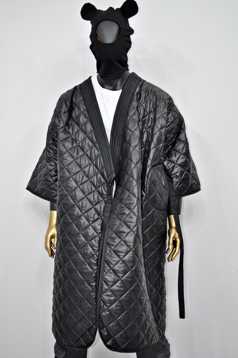 May include: A black quilted robe with a long, open front and a tie belt. The robe has a diamond pattern and is worn over a white t-shirt.