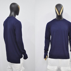 Puede incluir: Una camiseta de manga larga azul marino con agujeros para los pulgares en los puños. La camiseta tiene un corte holgado y una longitud ligeramente más larga en la espalda.