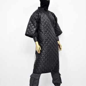 May include: A black quilted robe with a hood and ear flaps. The robe is worn over gray sweatpants with cargo pockets. The model is wearing black socks and black shoes.