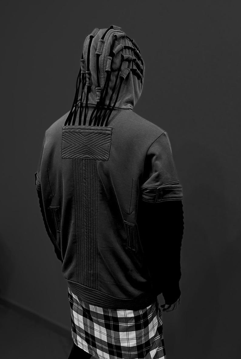 K&ouml;nnte beinhalten: Ein dunkelgrauer Kapuzenpullover mit einem einzigartigen Design, mit einer strukturierten Kapuze mit vertikalen Akzenten und einem strukturierten R&uuml;ckenteil. Der Kapuzenpullover hat eine Tasche an jedem &Auml;rmel und wird mit einem schwarz-wei&szlig; karierten Rock kombiniert.