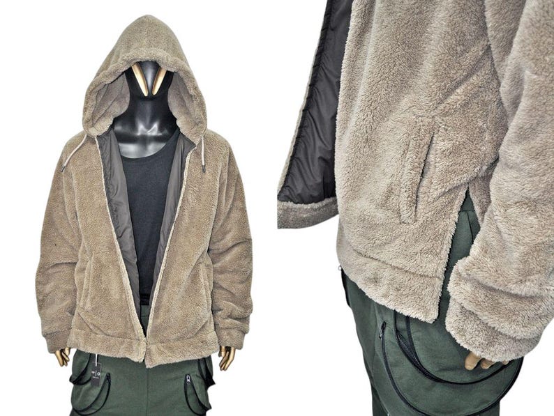 May include: A tan hooded jacket with a full zipper closure. The jacket has a soft, fuzzy texture and a black lining. The jacket is displayed on a mannequin with a black shirt underneath. The jacket has two side pockets and is paired with green cargo pants.