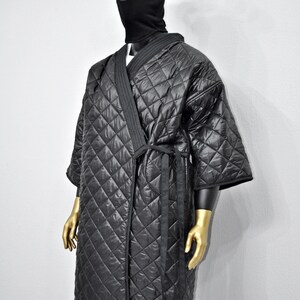 May include: A black quilted robe with a long sleeve and a tie belt. The robe has a diamond pattern and is worn by a mannequin with a black balaclava with bear ears.