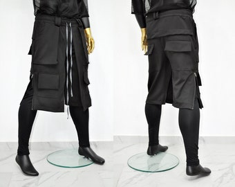 May include: Black cargo pants with multiple pockets and a wrap-around design. The pants feature a drawstring waist and a zipper detail on the side. The model is wearing black leggings and black shoes. The pants are displayed on a mannequin.