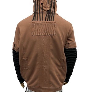 K&ouml;nnte beinhalten: Brauner Kapuzenpullover mit schwarzen Akzenten. Merkmale sind ein strukturiertes Design auf dem R&uuml;cken, schwarze gerippte &Auml;rmel und dekorative schwarze Kordeln an der Kapuze. Der Pullover hat eine einzigartige, futuristische &Auml;sthetik.