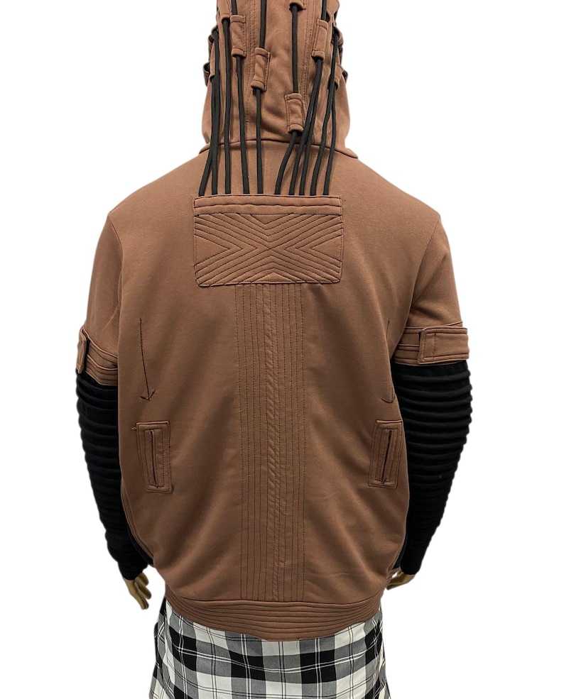K&ouml;nnte beinhalten: Brauner Kapuzenpullover mit schwarzen Akzenten. Merkmale sind ein strukturiertes Design auf dem R&uuml;cken, schwarze gerippte &Auml;rmel und dekorative schwarze Kordeln an der Kapuze. Der Pullover hat eine einzigartige, futuristische &Auml;sthetik.