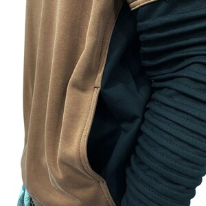 K&ouml;nnte beinhalten: Ein brauner Kapuzenpullover mit K&auml;ngurutasche und einem schwarzen &Auml;rmel. Der &Auml;rmel hat ein geripptes Design. Der Kapuzenpullover wird mit einer karierten Hose kombiniert.