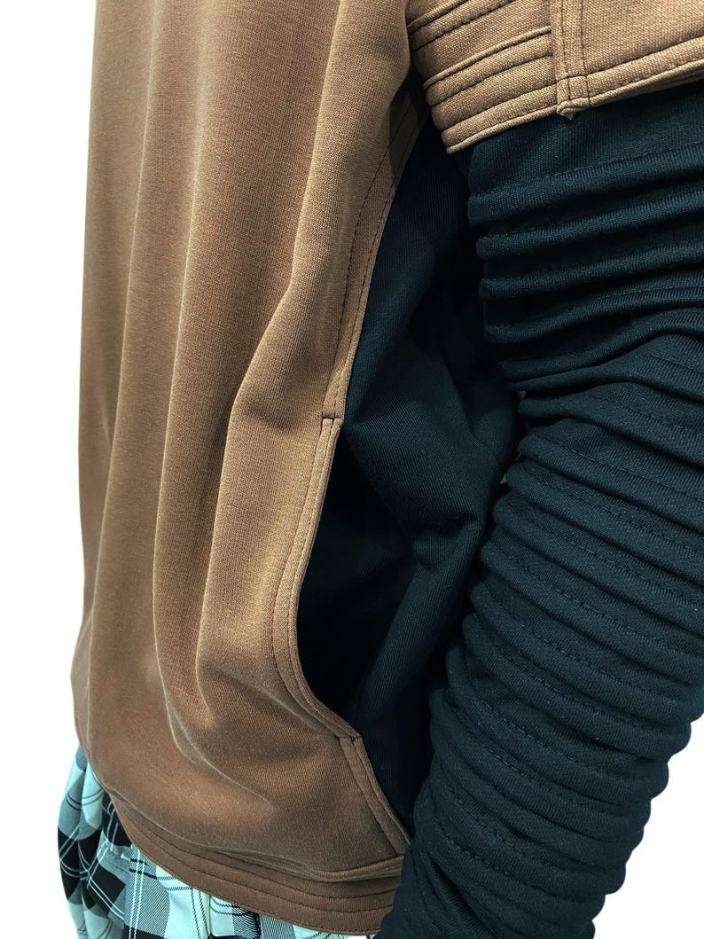 K&ouml;nnte beinhalten: Ein brauner Kapuzenpullover mit K&auml;ngurutasche und einem schwarzen &Auml;rmel. Der &Auml;rmel hat ein geripptes Design. Der Kapuzenpullover wird mit einer karierten Hose kombiniert.