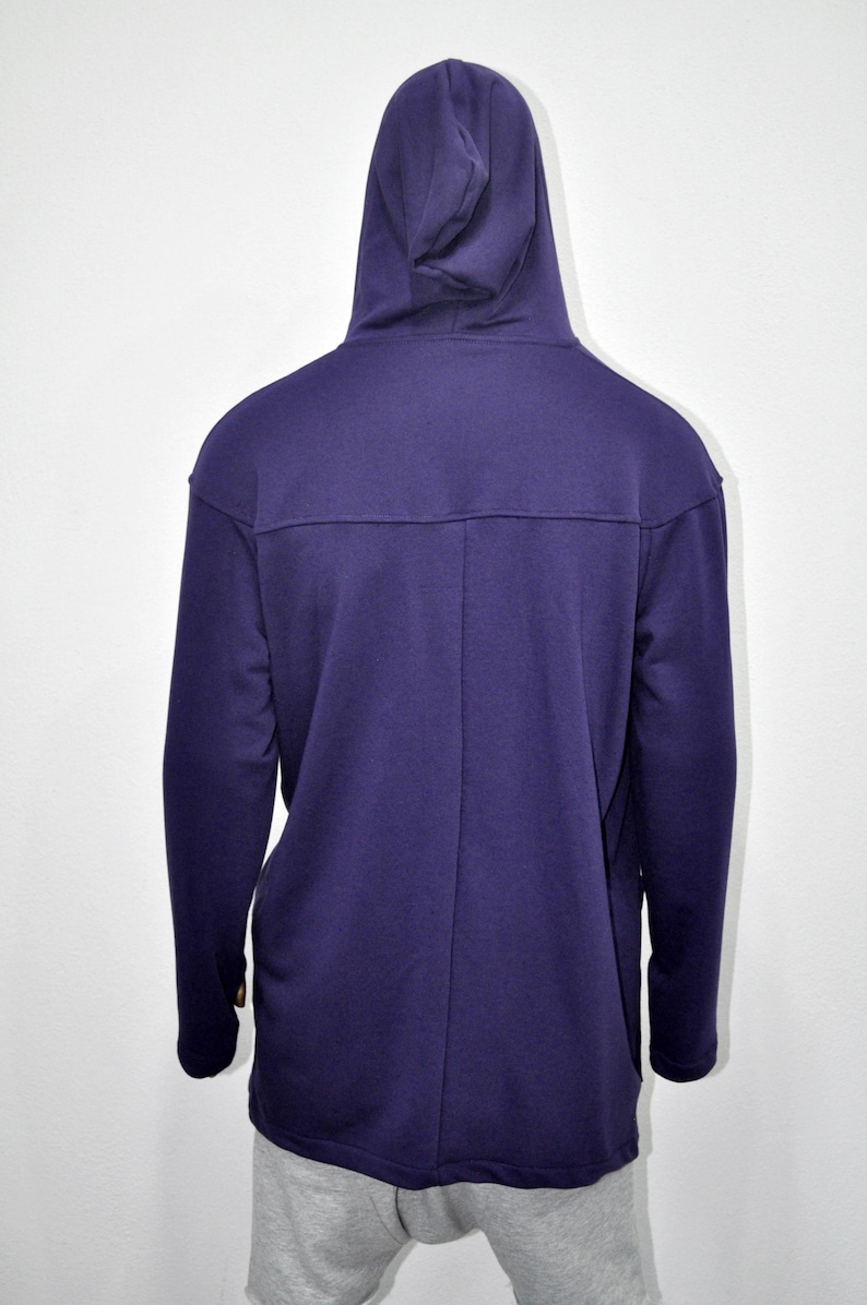 Puede incluir: Una sudadera con capucha de color p&uacute;rpura oscuro con capucha y mangas largas. La parte trasera de la sudadera con capucha es visible, mostrando un detalle de costura en la parte superior de la espalda. La parte inferior de la sudadera con capucha es visible, con pantalones de ch&aacute;ndal grises.