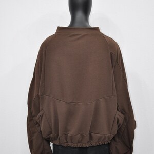 Puede incluir: Una sudadera marr&oacute;n de manga larga con cintura el&aacute;stica fruncida. La sudadera tiene un corte holgado y un cuello alto.