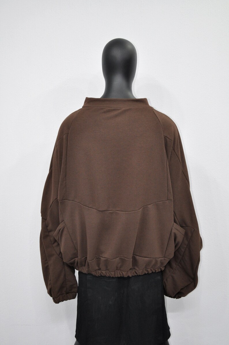 Puede incluir: Una sudadera marr&oacute;n de manga larga con cintura el&aacute;stica fruncida. La sudadera tiene un corte holgado y un cuello alto.