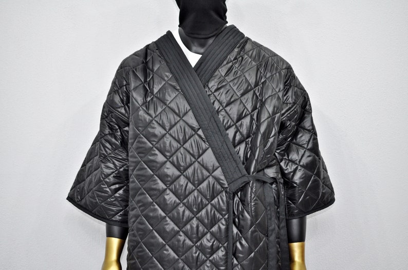 May include: A black quilted robe with a tie closure. The robe has a diamond pattern and is made of a shiny material.