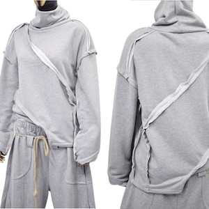 Könnte beinhalten: Ein grauer Pullover mit hohem Kragen und langen Ärmeln. Der Pullover hat ein einzigartiges Design mit weißen Nähten, die ein diagonales Muster auf der Vorder- und Rückseite bilden.