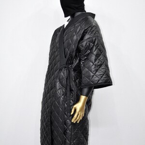 May include: A black quilted robe with a long sleeve and a tie belt. The robe is made of a soft, comfortable material and has a diamond pattern.