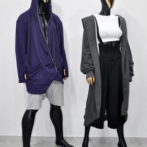 Puede incluir: Dos maniqu&iacute;es exhiben atuendos contempor&aacute;neos. Uno lleva una chaqueta con capucha morada con cremallera y pantalones cortos grises. El otro maniqu&iacute; viste un top corto blanco, pantalones negros de cintura alta con tirantes y una rebeca larga gris.