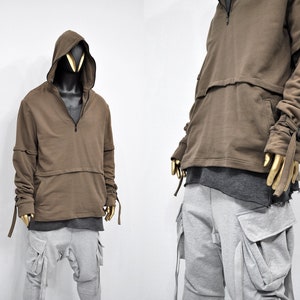May include: A brown hooded sweatshirt with a half-zip closure and long sleeves. The sleeves have long ties that can be tied at the wrist. The sweatshirt has a pocket on the front and a seam across the chest.