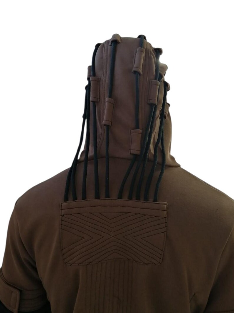 K&ouml;nnte beinhalten: Ein brauner Kapuzenpullover mit schwarzen Kordeln und Akzenten. Die Kapuze hat mehrere schwarze Kordeln mit braunen zylindrischen Akzenten. Auf der R&uuml;ckseite des Sweatshirts befindet sich ein gesticktes geometrisches Design und vertikale N&auml;hte.