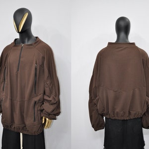 Puede incluir: Una sudadera marr&oacute;n con cremallera y bolsillos. La sudadera tiene un corte holgado y un cord&oacute;n en la parte inferior.