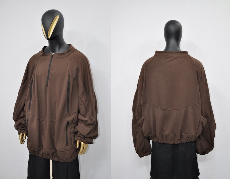 Puede incluir: Una sudadera marr&oacute;n con cremallera y bolsillos. La sudadera tiene un corte holgado y un cord&oacute;n en la parte inferior.