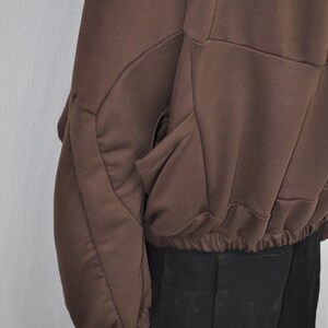 Puede incluir: Una sudadera marr&oacute;n con un dise&ntilde;o geom&eacute;trico &uacute;nico y una cintura con cord&oacute;n. La sudadera tiene un bolsillo grande en el lado izquierdo.