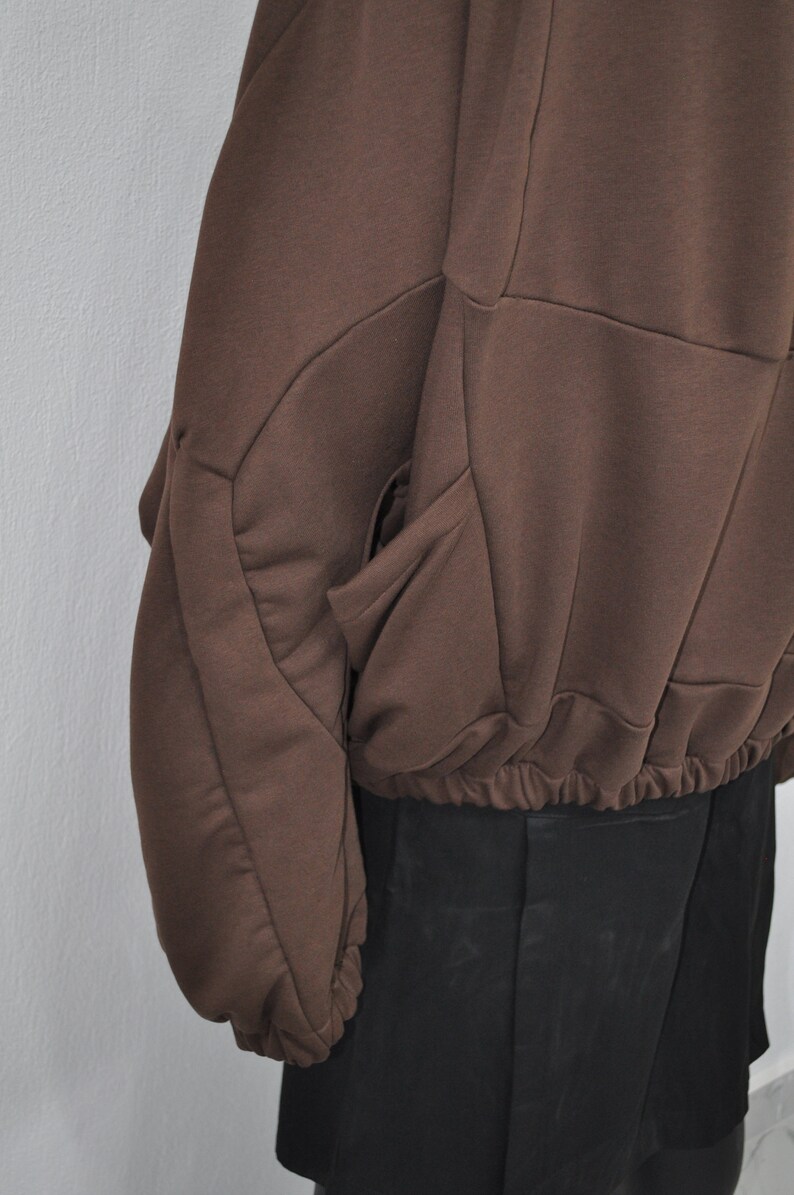 Puede incluir: Una sudadera marr&oacute;n con un dise&ntilde;o geom&eacute;trico &uacute;nico y una cintura con cord&oacute;n. La sudadera tiene un bolsillo grande en el lado izquierdo.