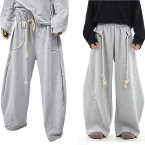 Könnte beinhalten: Graue Jogginghose mit Kordelzugbund und Seitentaschen. Die Jogginghose hat eine lockere Passform und ist aus einem weichen, bequemen Stoff gefertigt.