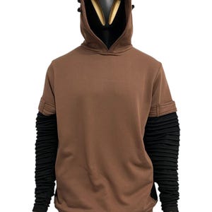 K&ouml;nnte beinhalten: Brauner Kapuzenpullover mit schwarzer Kapuze und &Auml;rmeln. Der Kapuzenpullover hat ein einzigartiges Design mit strukturierter Kapuze und &Auml;rmeln. Die &Auml;rmel sind lang und eng anliegend, und der Kapuzenpullover ist aus einem weichen Material gefertigt. Die Schaufensterpuppe tr&auml;gt einen karierten Rock.
