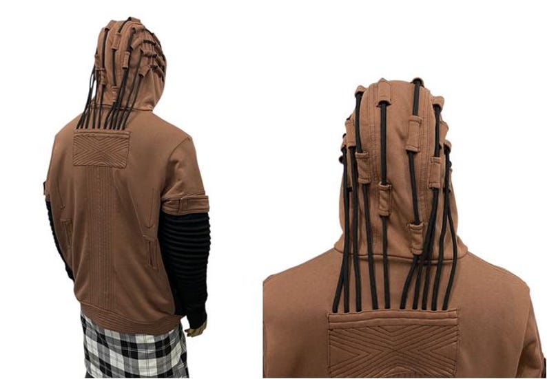 K&ouml;nnte beinhalten: Brauner Kapuzenpullover mit schwarzen Akzenten. Die Kapuze hat mehrere schwarze Kordeln, und die &Auml;rmel sind schwarz mit gerippten Details. Die R&uuml;ckseite des Sweatshirts hat ein strukturiertes Design. Die Person tr&auml;gt ein schwarz-wei&szlig;es Karomuster.