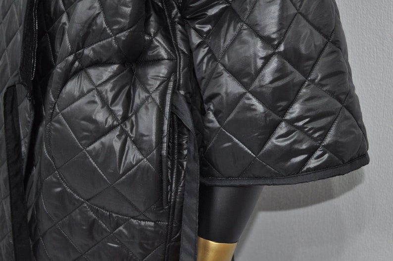 May include: Black quilted jacket with a diamond pattern. The jacket has a zipper closure and a stand-up collar.