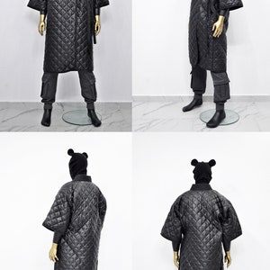 May include: A black quilted robe with a hood and ear flaps. The robe has a tie belt and is worn over grey pants.