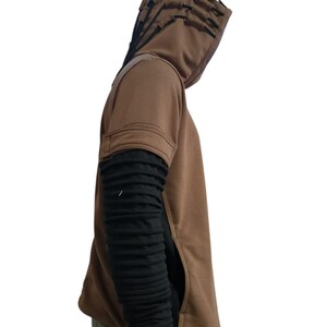 K&ouml;nnte beinhalten: Ein brauner Kapuzenpullover mit einem einzigartigen Design. Die Kapuze hat mehrere geschichtete Klappen. Die &Auml;rmel sind schwarz und strukturiert und kontrastieren mit dem braunen K&ouml;rper. Eine Tasche ist auf der Vorderseite sichtbar. Das Kleidungsst&uuml;ck ist ein l&auml;ssiger Stil.