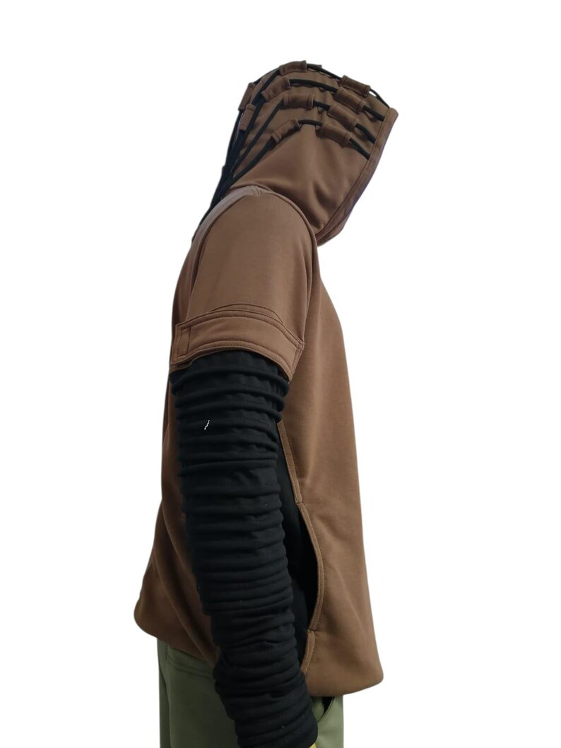 K&ouml;nnte beinhalten: Ein brauner Kapuzenpullover mit einem einzigartigen Design. Die Kapuze hat mehrere geschichtete Klappen. Die &Auml;rmel sind schwarz und strukturiert und kontrastieren mit dem braunen K&ouml;rper. Eine Tasche ist auf der Vorderseite sichtbar. Das Kleidungsst&uuml;ck ist ein l&auml;ssiger Stil.