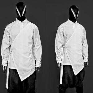 Könnte beinhalten: Zwei Mannequins tragen weiße langärmelige Hemden mit einem einzigartigen Wickeldesign. Die Hemden haben einen Kragen und sind in der Taille gebunden.