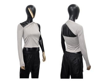 May include: A gray one-shoulder top with long sleeves. The top is cropped and has a draped design.
