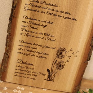 Könnte beinhalten: Ein Holzschild mit einem Gedicht über die Heimat, geschrieben in deutscher Sprache. Das Gedicht handelt von der Bedeutung der Heimat und wie sie ein Ort der Liebe und Freude ist. Das Schild ist mit einem Löwenzahnmuster verziert.