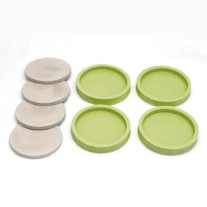May include: Set of six coasters, four are green and two are beige. The coasters are round and have a smooth surface.