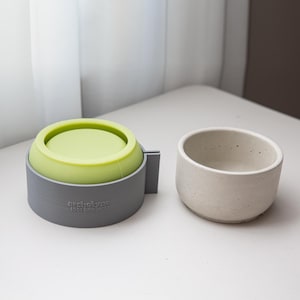 May include: A grey and green silicone mould for making concrete planters. The mould is in two pieces, with a removable top. The text "archetype 10oz twin mould" is printed on the bottom of the mould.