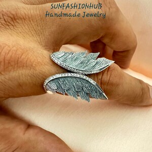 Puede incluir: Un anillo de plata con un dise&ntilde;o de pluma detallado. El anillo est&aacute; engastado con peque&ntilde;as piedras transparentes y tiene un acabado texturizado.