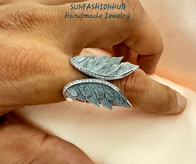 Puede incluir: Un anillo de plata con un dise&ntilde;o de pluma detallado. El anillo est&aacute; engastado con peque&ntilde;as piedras transparentes y tiene un acabado texturizado.