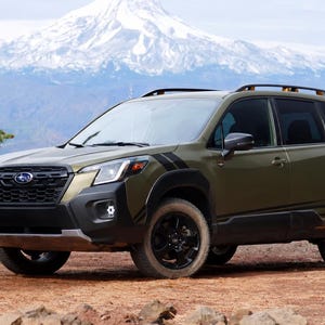May include: An olive green Subaru Forester SUV featuring black trim, black wheels, and black side decals. The vehicle has a roof rack, a black front grille with the Subaru emblem, and dark-tinted windows, positioned on a dirt surface.