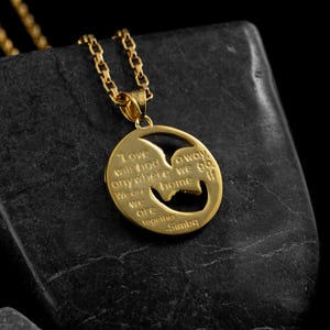 May include: A gold-colored pendant necklace with a circular charm. The charm features a cutout silhouette and engraved text that reads "Love will find a way anywhere we go if we are together Simba."