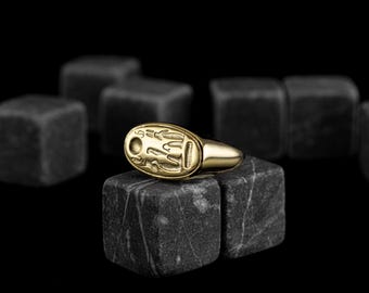 May include: A gold ring with an oval-shaped design featuring an intricate pattern. The ring is resting on a black stone surface.